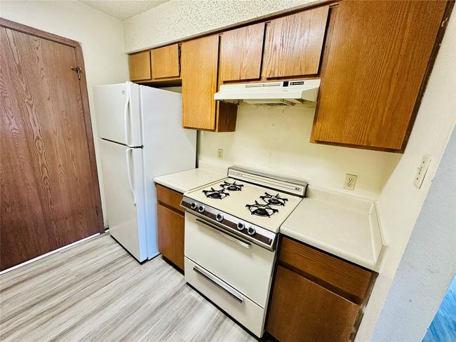 Kitchen featuring white appliances, under cabinet range hood, brown cabinetry, light countertops, and light wood-style floors | Image 10
