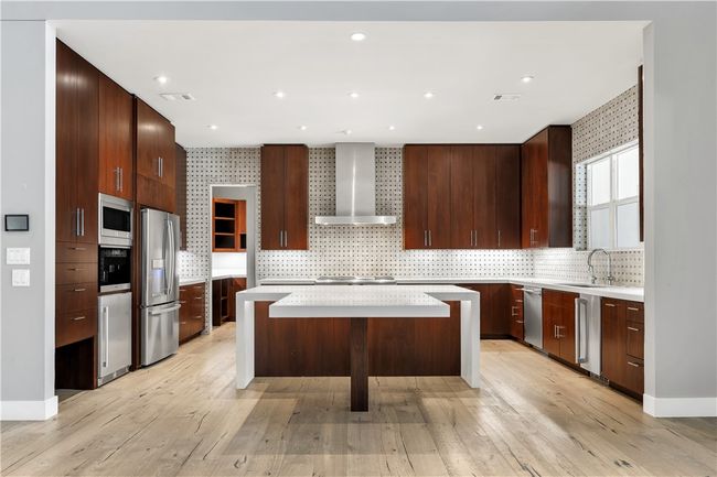 Kitchen featuring wall chimney range hood, stainless steel appliances, a kitchen island, light countertops, and decorative backsplash | Image 9