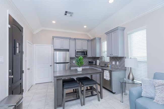 This modern kitchen features sleek gray cabinetry, stainless steel appliances, and a stylish island with seating. The room is brightened by ample natural light from large windows and complemented by contemporary decor. | Image 31