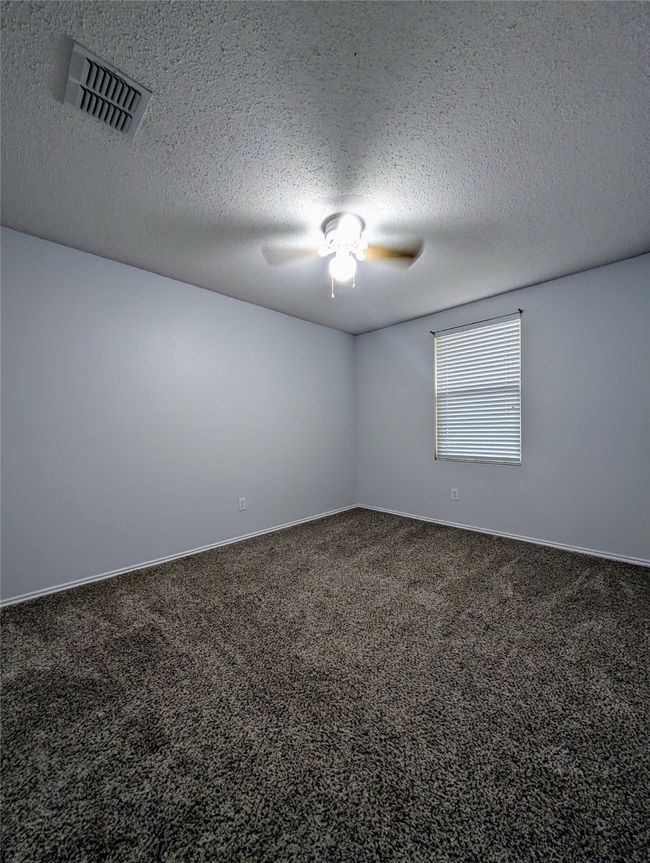 Carpeted empty room featuring a ceiling fan, a textured ceiling, and baseboards | Image 15