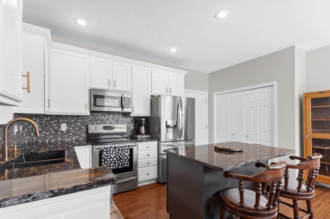 Enameled cabinetry, electric stove, granite countertops, and chic tile backsplash surround. | Image 22