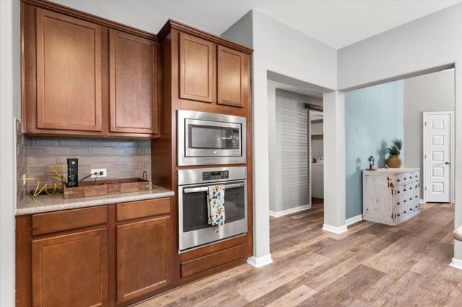 Kitchen featuring stainless steel appliances, light wood laminate floors, tasteful backsplash, light countertops, and baseboards | Image 10