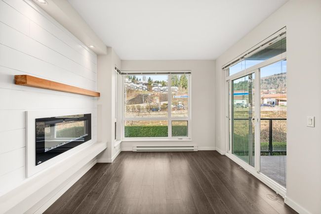 Unfurnished living room with baseboard heating, dark wood-style floors, and a glass covered fireplace | Image 10