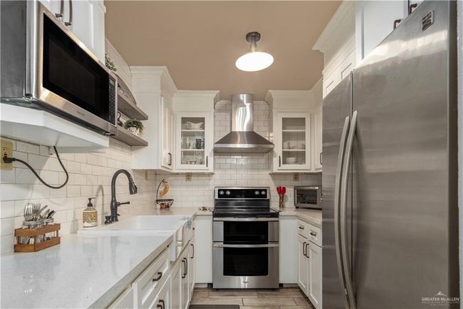 Kitchen with appliances with stainless steel finishes, wall chimney range hood, decorative backsplash, and white cabinets | Image 8