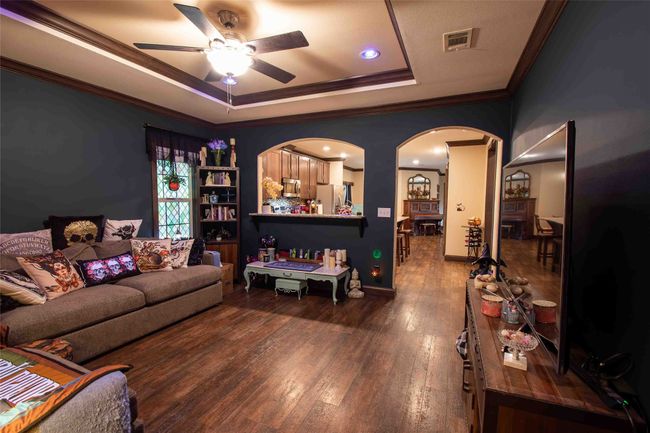 Second Living room with arched walkways, a raised ceiling, a ceiling fan, wood-type flooring, and crown molding | Image 18