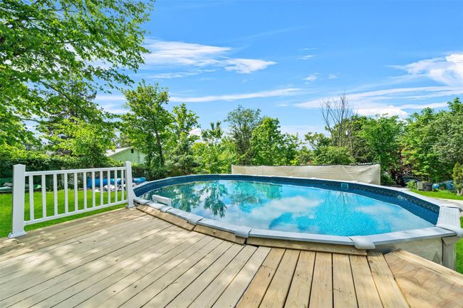 Outdoor pool with a wooden deck, a lawn, and view of scattered trees | Image 28