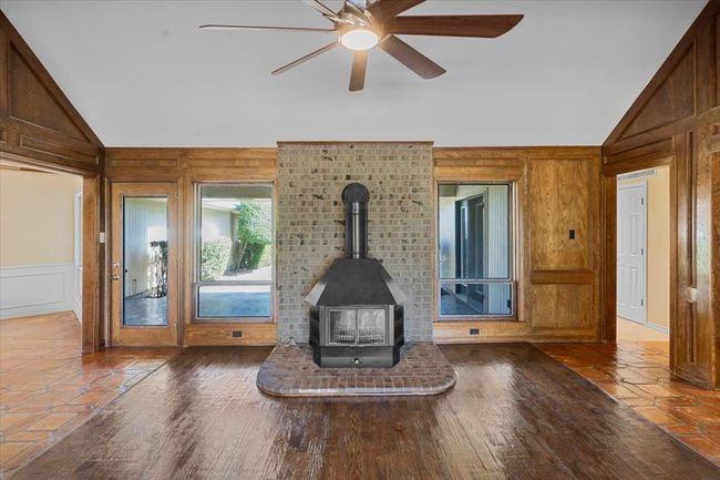 Unfurnished living room with wooden walls, a wood stove, lofted ceiling, ceiling fan, and wood-type flooring | Image 2