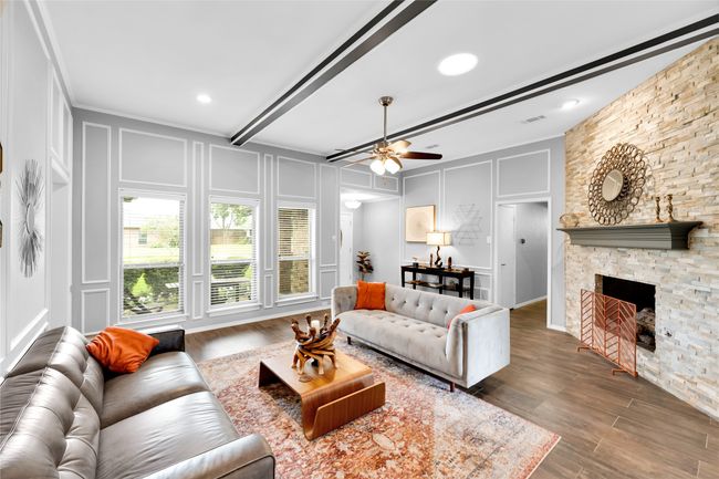 Living room with a decorative wall, ceiling fan, wood finished floors, a stone fireplace, and beamed ceiling | Image 8