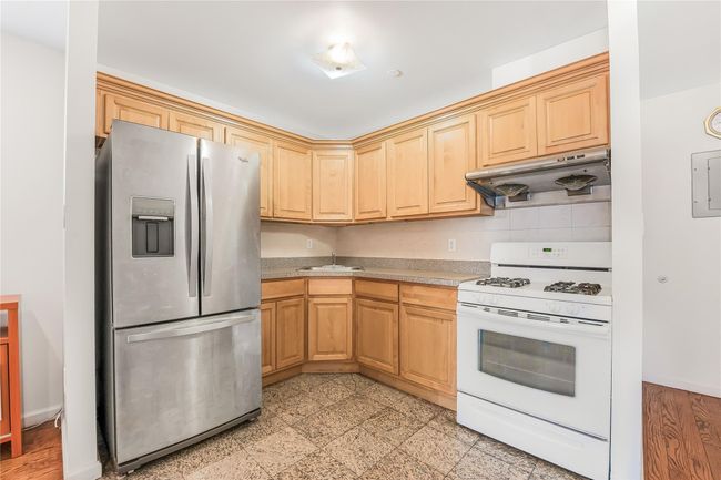 Kitchen featuring stainless steel fridge, white range with gas stovetop, extractor fan, light countertops, and light brown cabinetry | Image 4