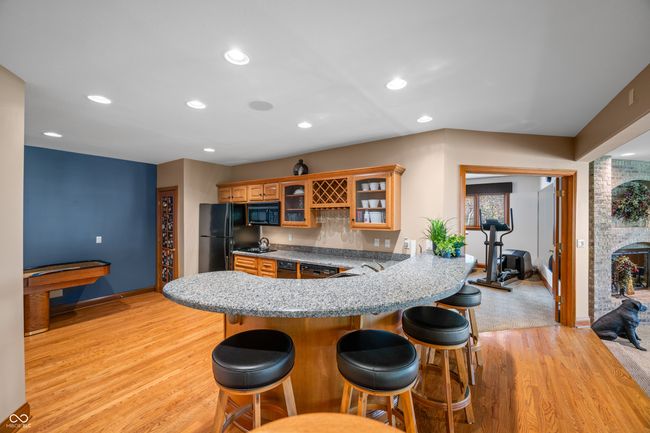 Bar kitchen with a kitchen breakfast bar, brown cabinetry, black appliances, a peninsula, and light wood-style flooring | Image 65