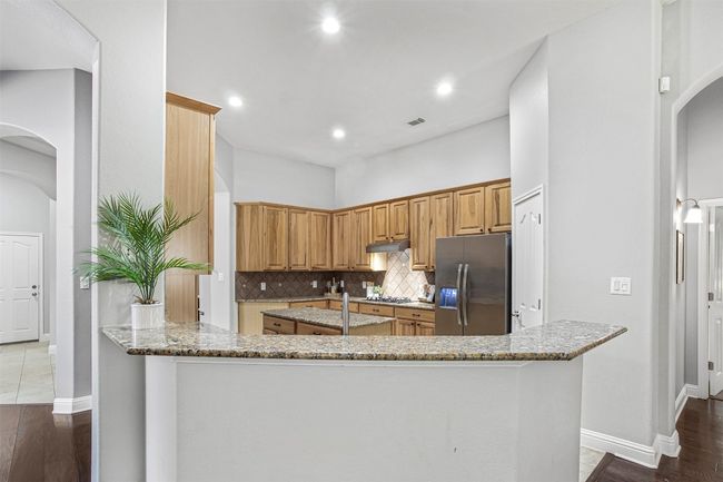 Kitchen featuring stainless steel appliances, arched walkways, light stone counters, under cabinet range hood, and recessed lighting | Image 14