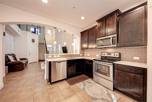 Kitchen with stainless steel appliances, arched walkways, dark brown cabinets, a sink, and backsplash | Image 5