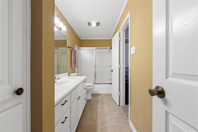 Full bath featuring tile patterned floors, shower / bath combination with glass door, toilet, crown molding, and vanity | Image 24