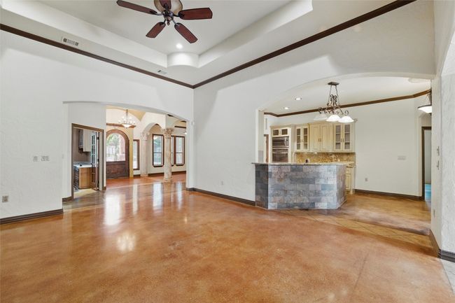 Unfurnished living room with arched walkways, a chandelier, a ceiling fan, crown molding, and baseboards | Image 9