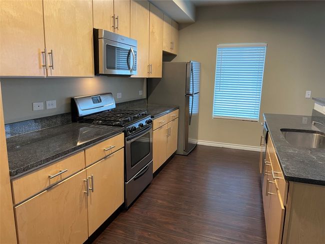 Kitchen with appliances with stainless steel finishes, dark wood-type flooring, and dark stone countertops | Image 12