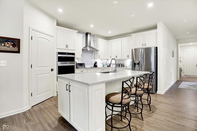Modern kitchen with range hood, stainless steel appliances, tile backsplash, large pantry & kitchen breakfast bar | Image 6