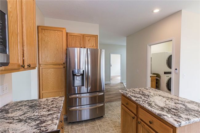 Kitchen with light tile patterned floors, stainless steel fridge with ice dispenser, light stone counters, stacked washer / drying machine, and a center island | Image 22