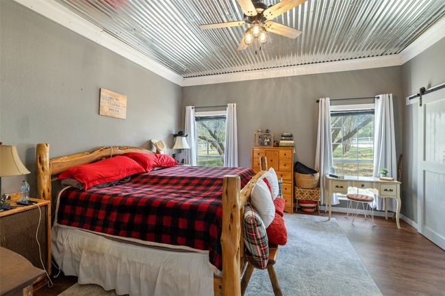 Bedroom featuring wood finished floors, a barn door, ornamental molding, wood ceiling, and ceiling fan | Image 21
