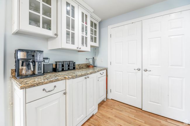 Kitchen featuring light wood finished floors, glass insert cabinets, white cabinetry, and light stone countertops | Image 9