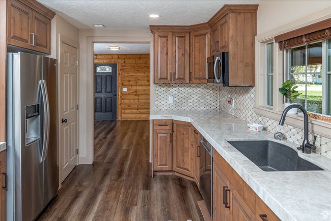 Kitchen featuring appliances with stainless steel finishes, dark wood finished floors, brown cabinetry, a textured ceiling, and backsplash | Image 20