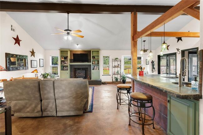 Living room with a brick fireplace, concrete flooring, ceiling fan, and plenty of natural light | Image 8