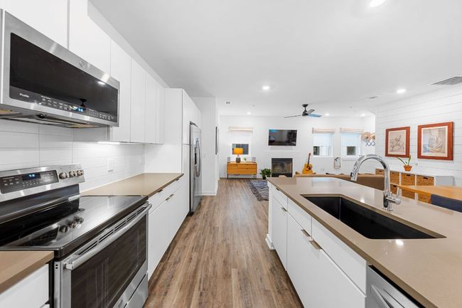 Kitchen featuring a sink, white cabinetry, tasteful backsplash, wood finished floors, and appliances with stainless steel finishes | Image 15