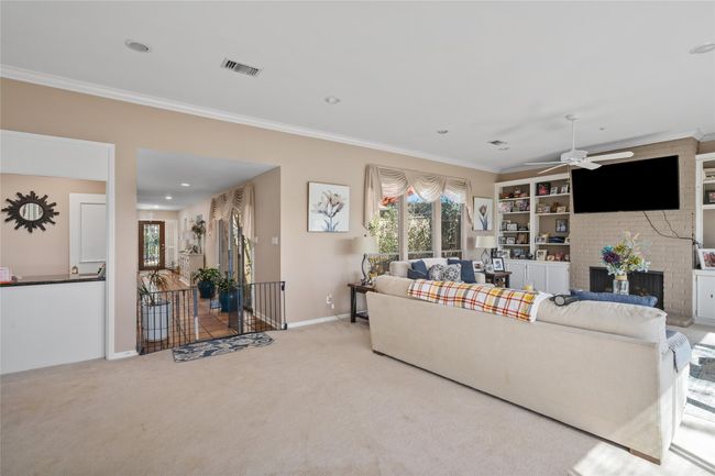 This spacious living area offers a cozy yet open feel, featuring a brick fireplace framed by built-in shelving for storage and display. Large windows allow for abundant natural light, while the neutral color palette and plush carpeting create a welcoming atmosphere. The room seamlessly connects to the foyer and kitchen, enhancing the home's flow. | Image 15
