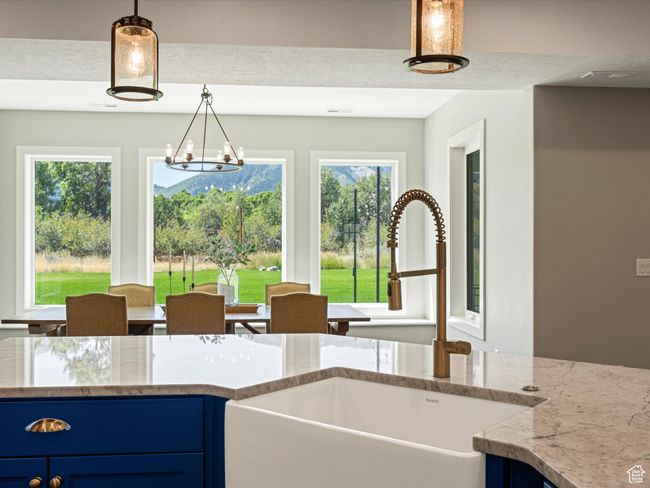 Kitchen featuring a sink, blue cabinetry, light stone countertops, pendant lighting, and a chandelier | Image 13