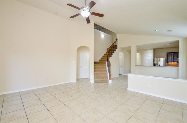 This spacious living area features high ceilings, neutral tile flooring, and a ceiling fan. An open staircase leads to the upper level, and the room flows into a modern kitchen with stainless steel appliances and dark wood cabinetry. Perfect for comfortable family living. | Image 10