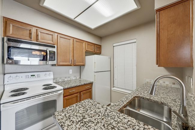 Kitchen featuring white appliances, brown cabinets, and light stone counters | Image 13