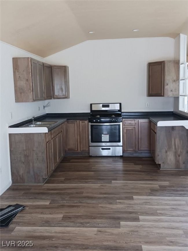 Kitchen featuring dark countertops, dark wood-type flooring, stainless steel range with gas stovetop, vaulted ceiling, and a sink | Image 16