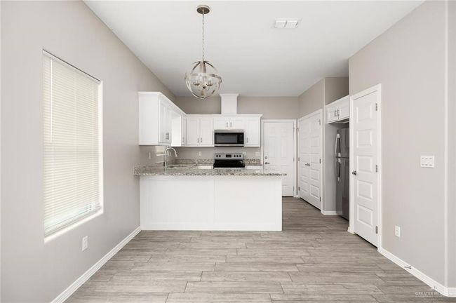 Kitchen featuring stainless steel appliances, a peninsula, a chandelier, and light wood-style floors | Image 6