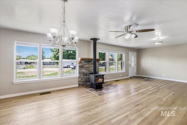 Unfurnished living room featuring a wood stove, light wood-type flooring, a chandelier, and a ceiling fan | Image 24
