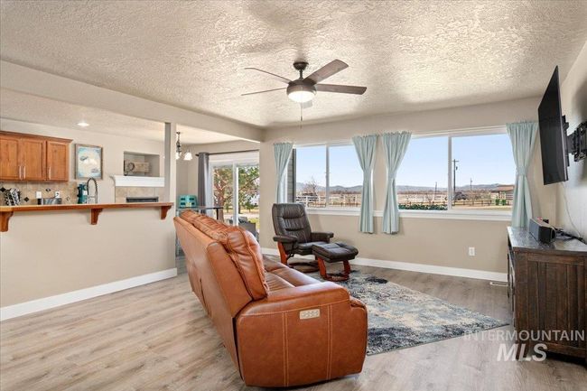 Living area with ceiling fan, light wood-style floors, a textured ceiling, and a tile fireplace | Image 5