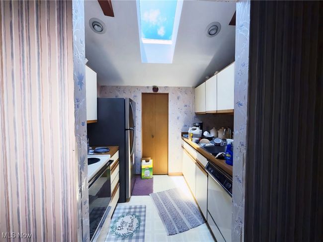 Kitchen featuring white appliances, wallpapered walls, white cabinetry, and a skylight | Image 17