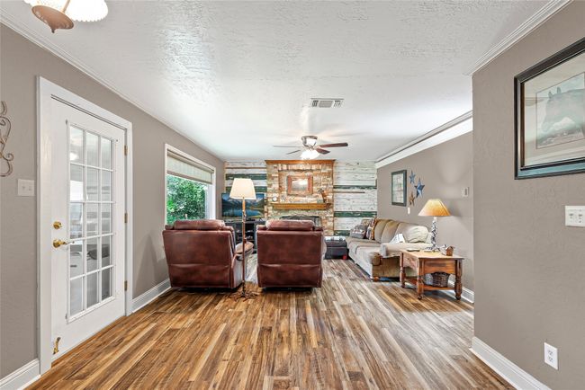 Living room with wood-type flooring, ceiling fan, a textured ceiling, crown molding, and a fireplace | Image 11