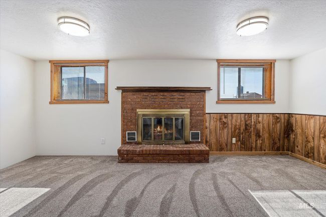 Unfurnished living room with carpet, a textured ceiling, plenty of natural light, a brick fireplace, and wood walls | Image 27