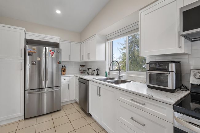 Kitchen featuring light tile patterned floors, a sink, white cabinets, appliances with stainless steel finishes, and backsplash | Image 6