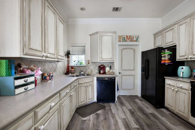 Kitchen featuring black appliances, cream cabinetry, light countertops, decorative backsplash, and ornamental molding | Image 12