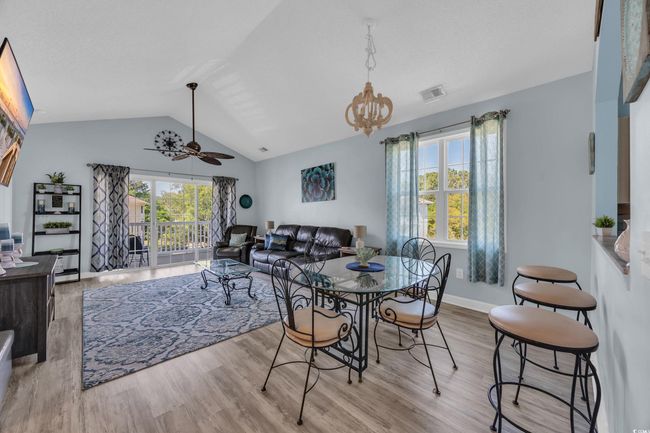 Dining area with lofted ceiling, wood finished floors, visible vents, baseboards, and ceiling fan with notable chandelier | Image 12