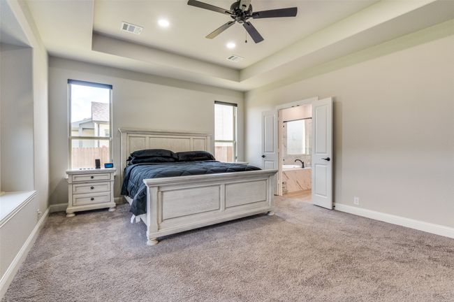 Carpeted bedroom featuring a tray ceiling, multiple windows, recessed lighting, ensuite bathroom, and a ceiling fan | Image 25