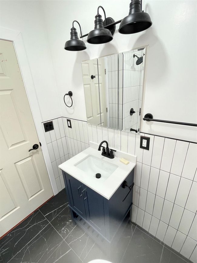 Full bath featuring tile walls, marble finish flooring, vanity, a tile shower, and wainscoting | Image 8