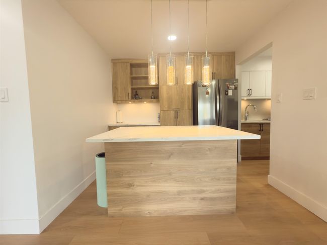 Kitchen with freestanding refrigerator, a sink, modern cabinets, light wood-type flooring, and a center island | Image 8