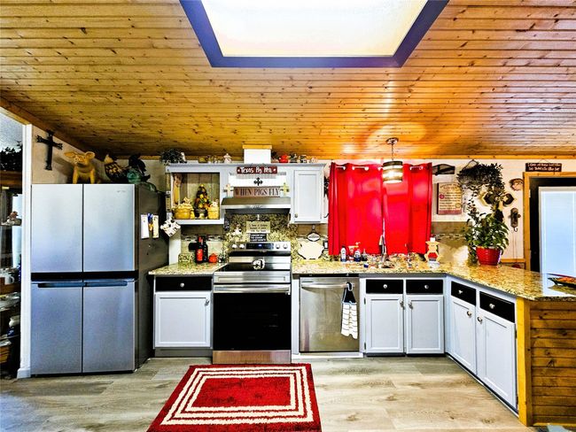 Kitchen with stainless steel appliances, a peninsula, wooden ceiling, light wood-type flooring, and light stone countertops | Image 5