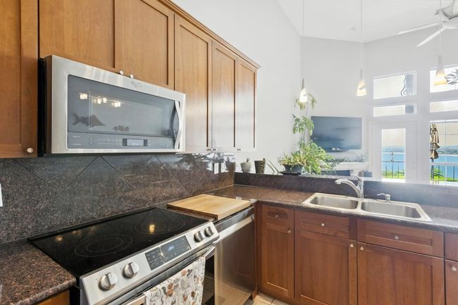 Kitchen with stainless steel appliances, backsplash, dark countertops, brown cabinets, and a towering ceiling | Image 14