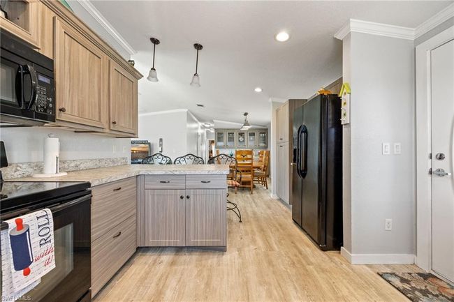 Kitchen with light wood-style floors, crown molding, black appliances, a peninsula, and light countertops | Image 8