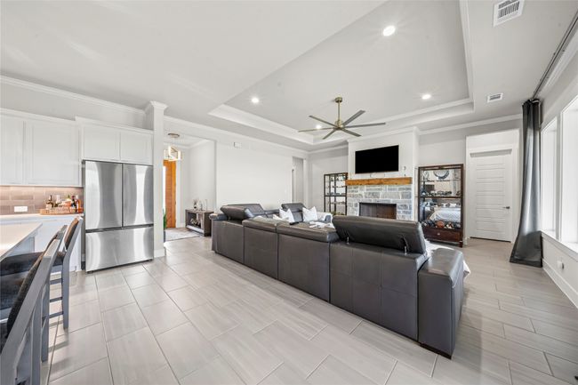 Living area with ornamental molding, a ceiling fan, a stone gas starting fireplace, a raised ceiling, and recessed lighting | Image 9