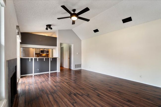Unfurnished living room featuring a ceiling fan, dark wood-type flooring, lofted ceiling, a fireplace, and a textured ceiling | Image 9