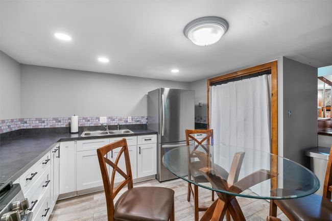 Kitchen with stainless steel appliances, a sink, dark countertops, white cabinets, and light wood-type flooring | Image 4