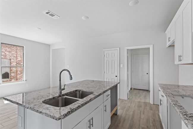Kitchen with sink, white cabinetry, light stone counters, and an island with sink | Image 5